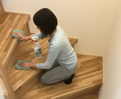 階段に膝をついて、雑巾とスプレー式洗剤で木製階段を丁寧に拭き掃除している女性